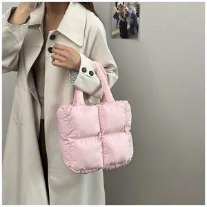 Close-up of a soft pink quilted puffer tote bag held by a model in a trench coat