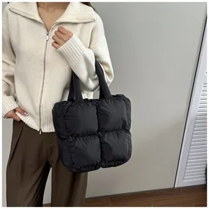 Detail view of a black quilted puffer tote bag styled with a beige winter sweater