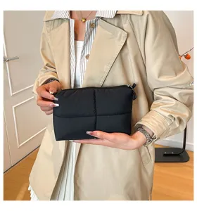 Schwarze gesteppte Kosmetiktasche, gehalten von einer Person im beigen Mantel.