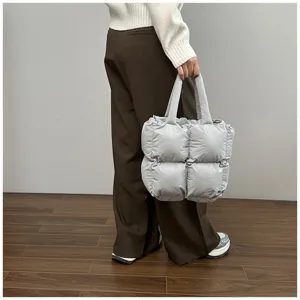 Close-up of a stylish silver quilted padded tote bag held by a person in a minimalist setting