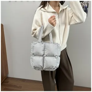 Close-up of a grey quilted puffy tote bag held by a model in a casual setting