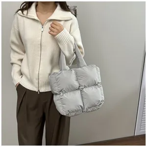 Close-up of a light grey padded tote bag styled with a white knit sweater for winter outfits.