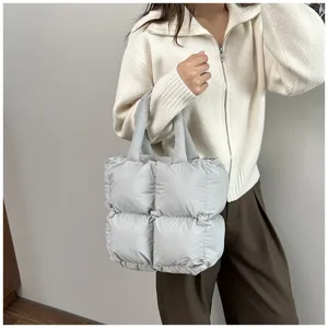 Light grey puffer tote bag held by a model wearing a stylish white knit sweater