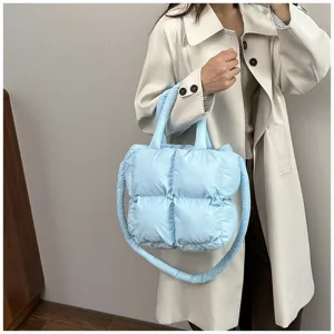 Light blue padded puffer tote bag held by a model wearing a stylish autumn trench coat