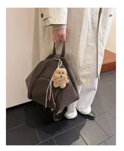 Detail view of a dark brown minimalist women backpack with a cute bear plush charm