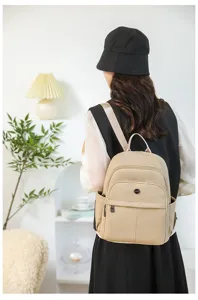 Back view of a stylish khaki textured backpack worn by a model in an indoor setting.