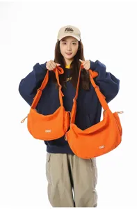 Model holding large and small orange crossbody dumpling bags for size comparison
