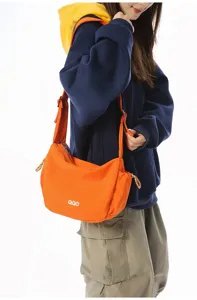 Detail view of the orange crossbody dumpling bag worn by a model in casual street style.