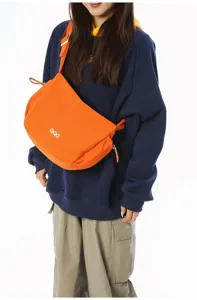 Orange dumpling crossbody bag for travel shown on a model in a navy hoodie.