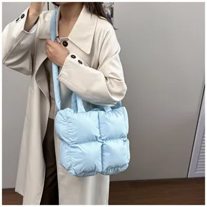 Light blue quilted puffer tote bag shown on a model wearing a stylish beige trench coat.