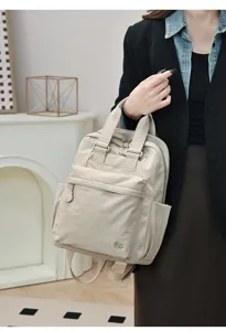 Close-up detail of casual beige nylon backpack showing front pocket, metal logo and handle.