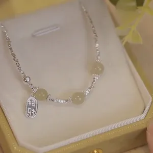 Gros plan d'une chevillère en perles d'argent avec un charme de prospérité gravé