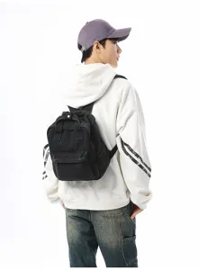 Rear view of a casual black washed denim backpack worn by a model in a white hoodie.
