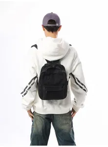 Detail back view of a minimalist black washed denim mini backpack worn over a white hoodie
