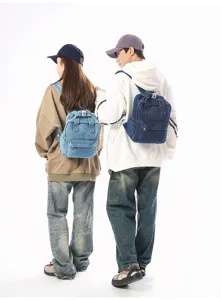 Back view of two models wearing small vintage washed denim backpacks in blue shades