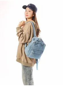 Detailed view of washed denim small backpack worn by model against white background