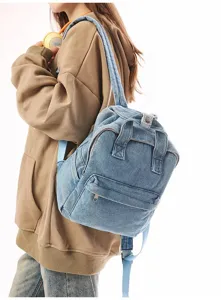 Back view of a casual washed denim backpack worn by a female model in a brown hoodie