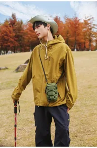 Man in mosterdjasje draagt een kleine groene tactische geruite crossbody tas buiten.