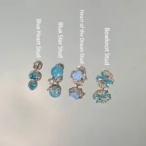 Selection of four blue crystal and zircon stud earrings on a reflective surface