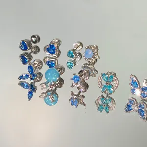 Close-up of sparkling blue rhinestone stud earrings in butterfly and heart shapes.