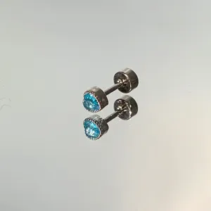 Detailed macro view of heart-shaped silver stud earring with bright blue stone on mirror
