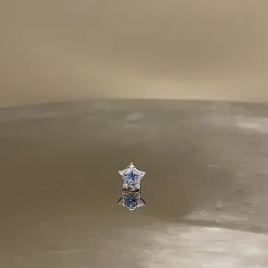 Detailed macro view of a silver star ear stud featuring a sparkling blue gemstone center