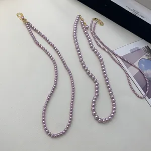 Detail view of three purple pearl necklaces with gold clasps on a minimalist background.