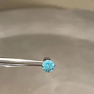 Detailed close-up of a sparkling sea blue sapphire round stud earring held by tweezers