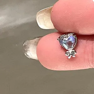 Close-up of a heart-shaped sapphire blue ear stud with a tiny silver bow detail