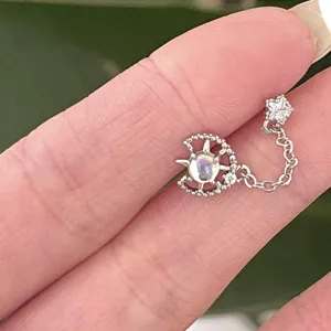 Macro detail of a delicate silver star and moon chain earring held for size reference