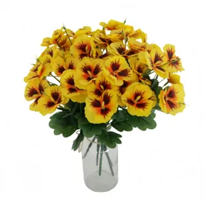 Close-up detail of artificial yellow pansy flowers bouquet with green leaves in a glass vase.