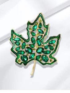 Primer plano de un broche de hoja de arce dorado hueco con cristales de color verde esmeralda