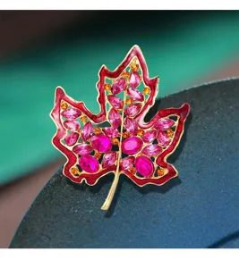 Primer plano de un elegante broche de hoja de arce chapado en oro con cristales rosa y naranja