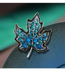 Vista detallada de un broche de hoja de arce plateado con cristalli azules vibrantes