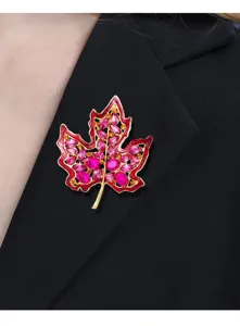 Vista detallada de un broche de hoja de arce con cristales magenta en una chaqueta.