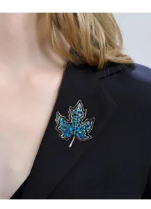 Detalle de un broche de hoja de arce con cristales azules en una solapa de chaqueta negra.