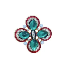 Vue détaillée d'une broche croix de style palais avec verre vert et émail rouge