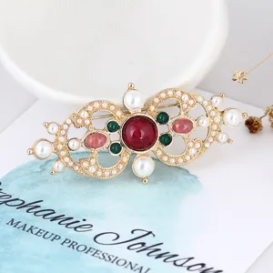Close-up of vintage baroque brooch with red gems and pearls on a white card.
