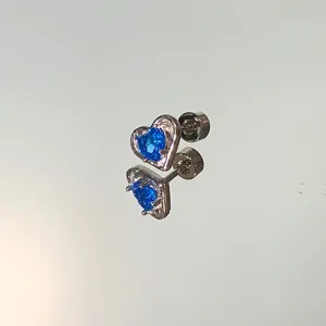 Detailed macro view of heart-shaped silver stud earring with blue gemstone inlay.