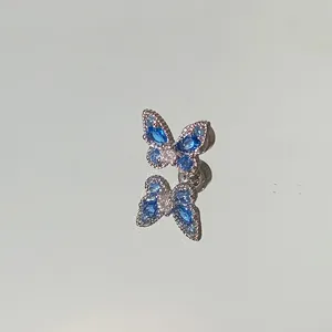 Close-up of a sparkling blue butterfly stud earring with clear reflections on a mirror surface.