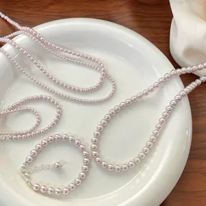 Elegant rose pink simulated pearl necklace and bracelet set on a white ceramic plate