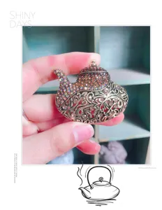Detailaufnahme einer Vintage-Teekanne-Brosche mit funkelnden bernsteinfarbenen Strasssteinen