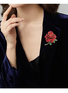 Detailansicht einer eleganten roten Rosenbrosche mit Strass auf einem blauen Samtblazer.