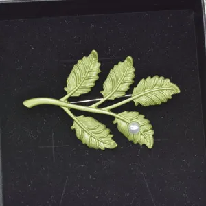 Primer plano de un broche de hoja lacado verde vintage con una perla blanca