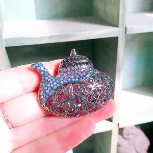Eleganter Teekannen-Brosche mit lila und blauen Strasssteinen auf schwarzem Metall
