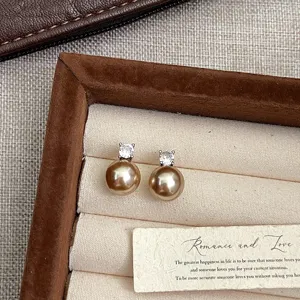 Primer plano de pendientes de perlas champán con circonita en un joyero elegante.
