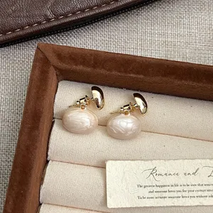 Detalle macro de elegantes pendientes de perlas de esmalte crema con detalles dorados.