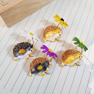 Detailed view of colorful enamel hedgehog brooches holding daisy flowers on paper