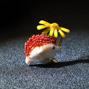Close-up detail of a cute hedgehog enamel brooch holding a bright yellow daisy flower