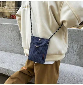 Dettaglio di una borsa a tracolla blu a scacchi per smartphone su un maglione crema.